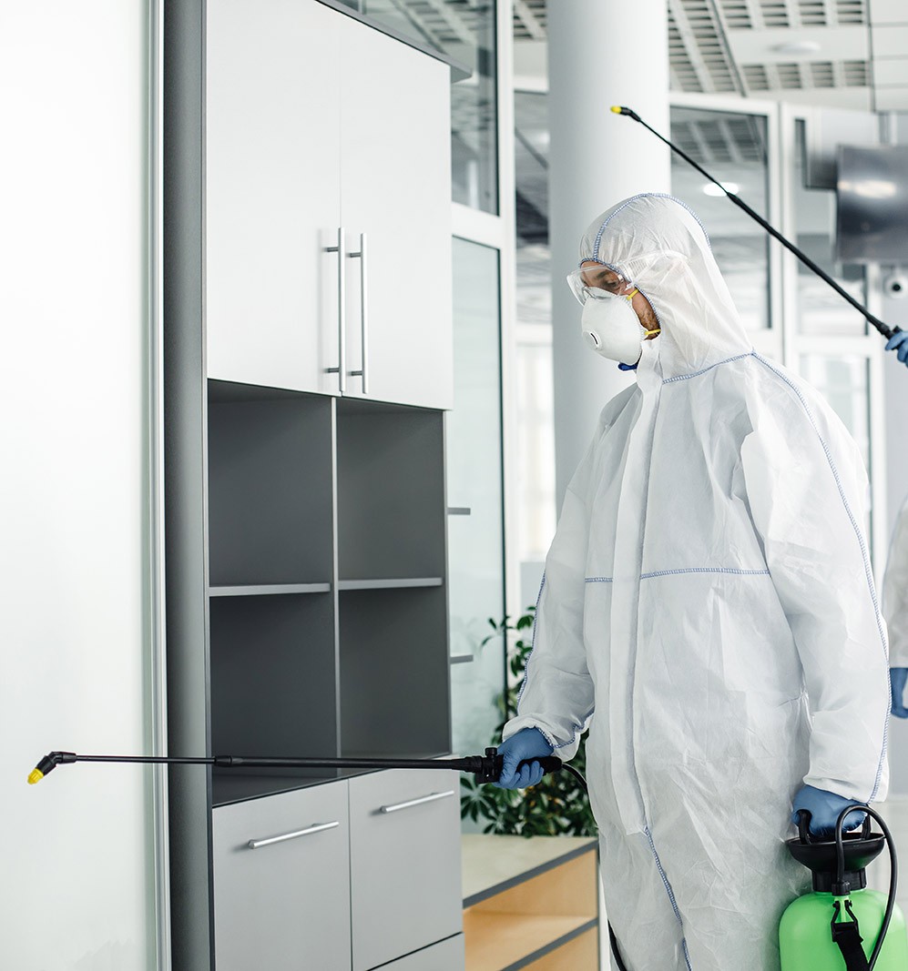 Professional disinfection of room and furniture during coronavirus epidemic. Men in hazmat suits, protective masks, goggles and with sprayer, cleans office with chemical